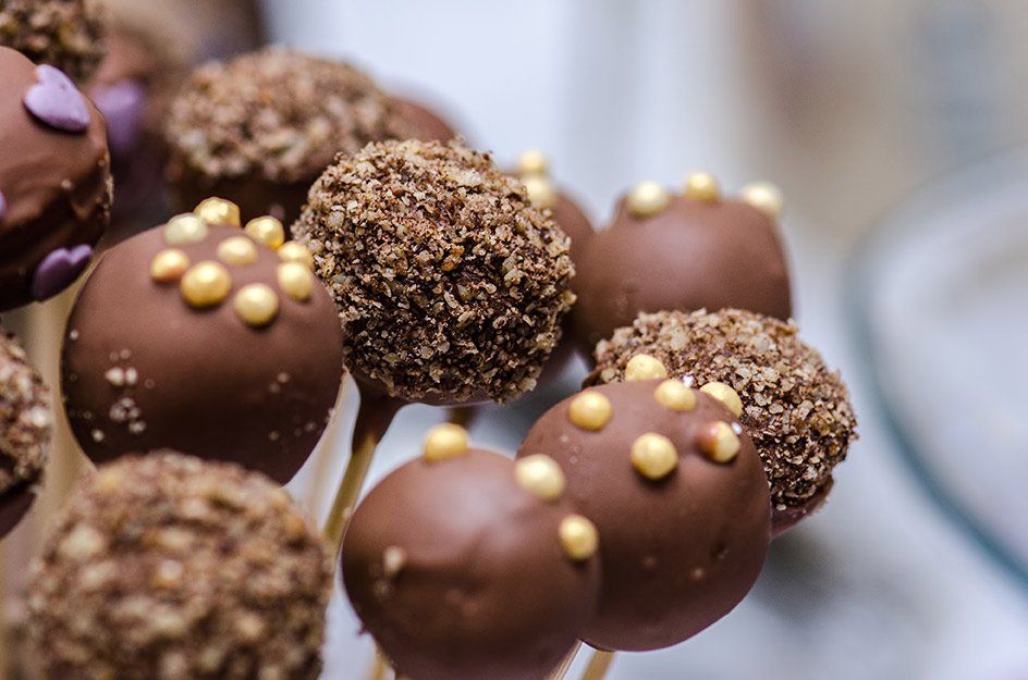 A bunch of chocolate cake pops on sticks on a table.