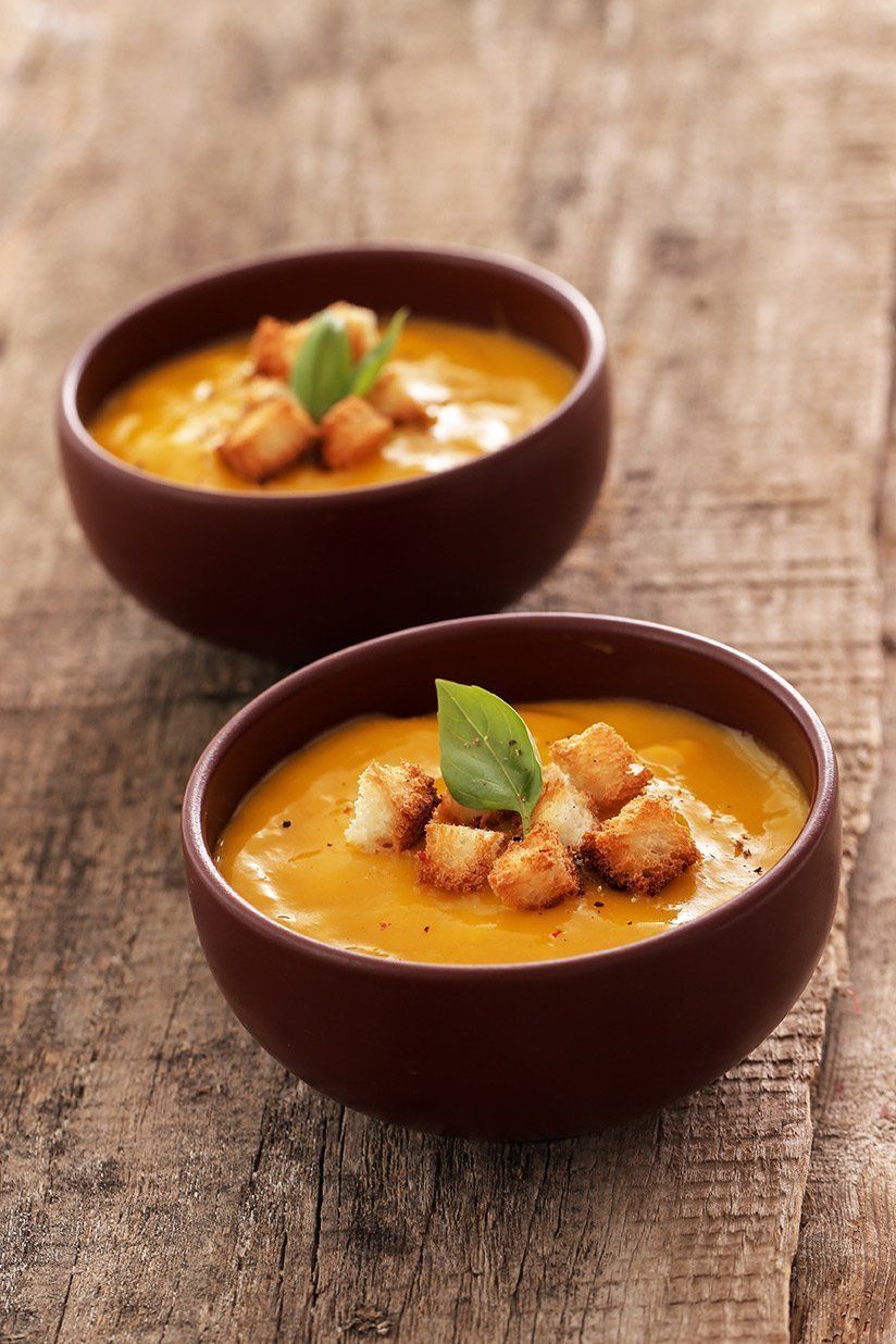 Two bowls of soup with croutons and basil on a wooden table.