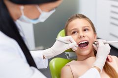 A young girl is sitting in a dental chair getting her teeth examined by a dentist.