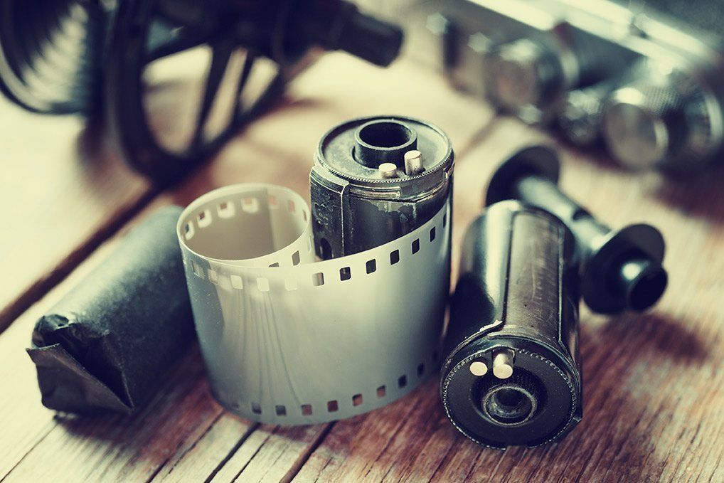 Three rolls of film are sitting on a wooden table next to a camera.