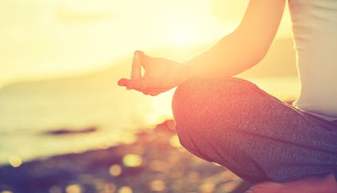 Een vrouw zit in lotushouding op een yogamat naast kaarsen.