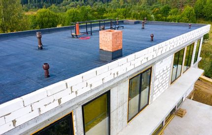Flat-roof building with white walls and rooftop vents surrounded by green trees