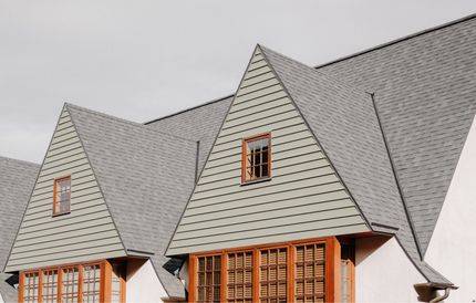 Gray shingle-roofed house with steep gables and dormer windows under a cloudy sky