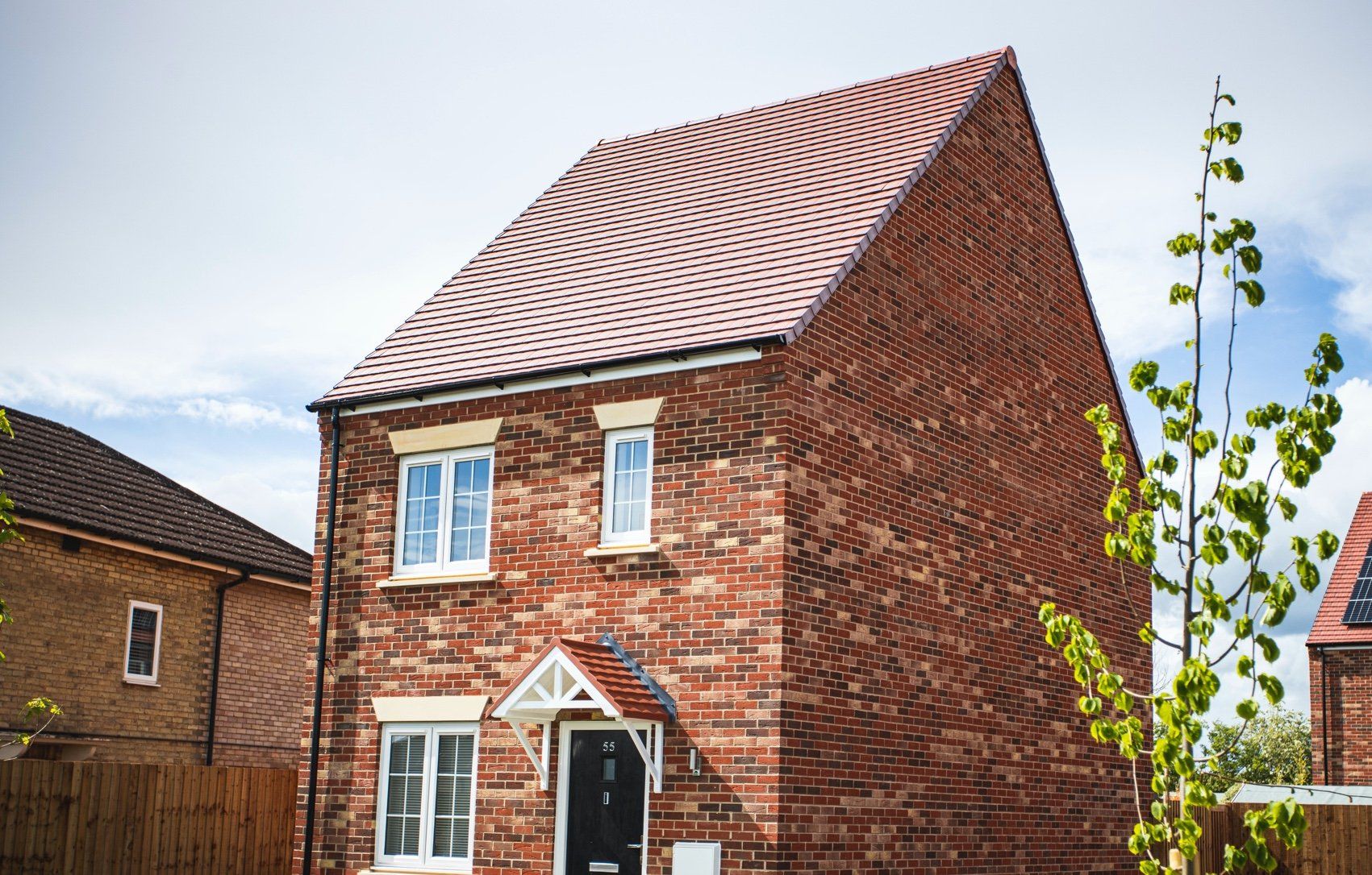 A brick house with a red roof and white windows is sitting in a residential area.