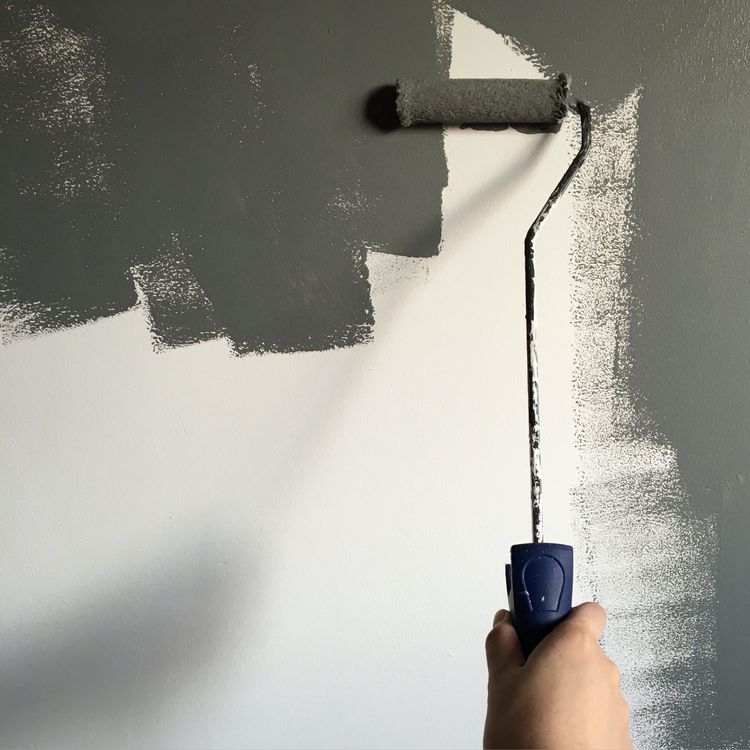 Dipingere a mano una parete bianca con vernice grigio scuro usando un rullo