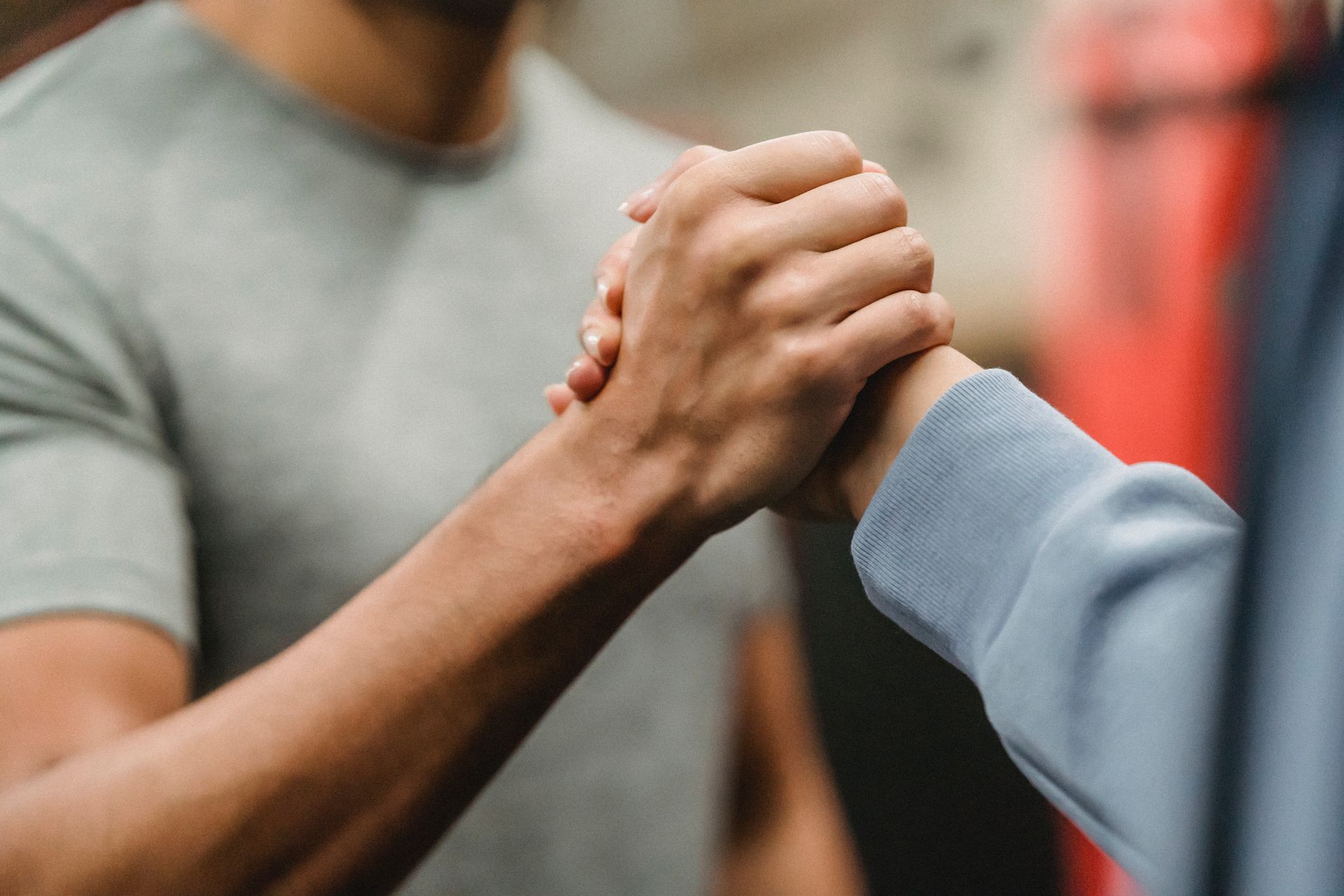 Two people clasping hands in a supportive handshake, one in a gray shirt and one in a blue sleeve.