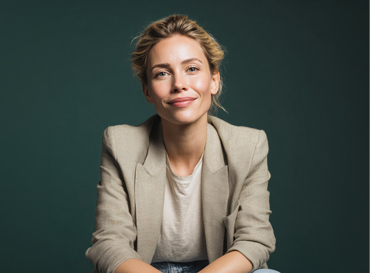 Smiling woman in a beige blazer seated against a dark green background