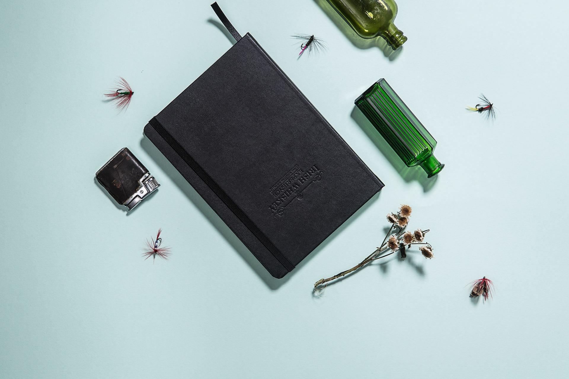 A black notebook is surrounded by bottles and flies on a table.