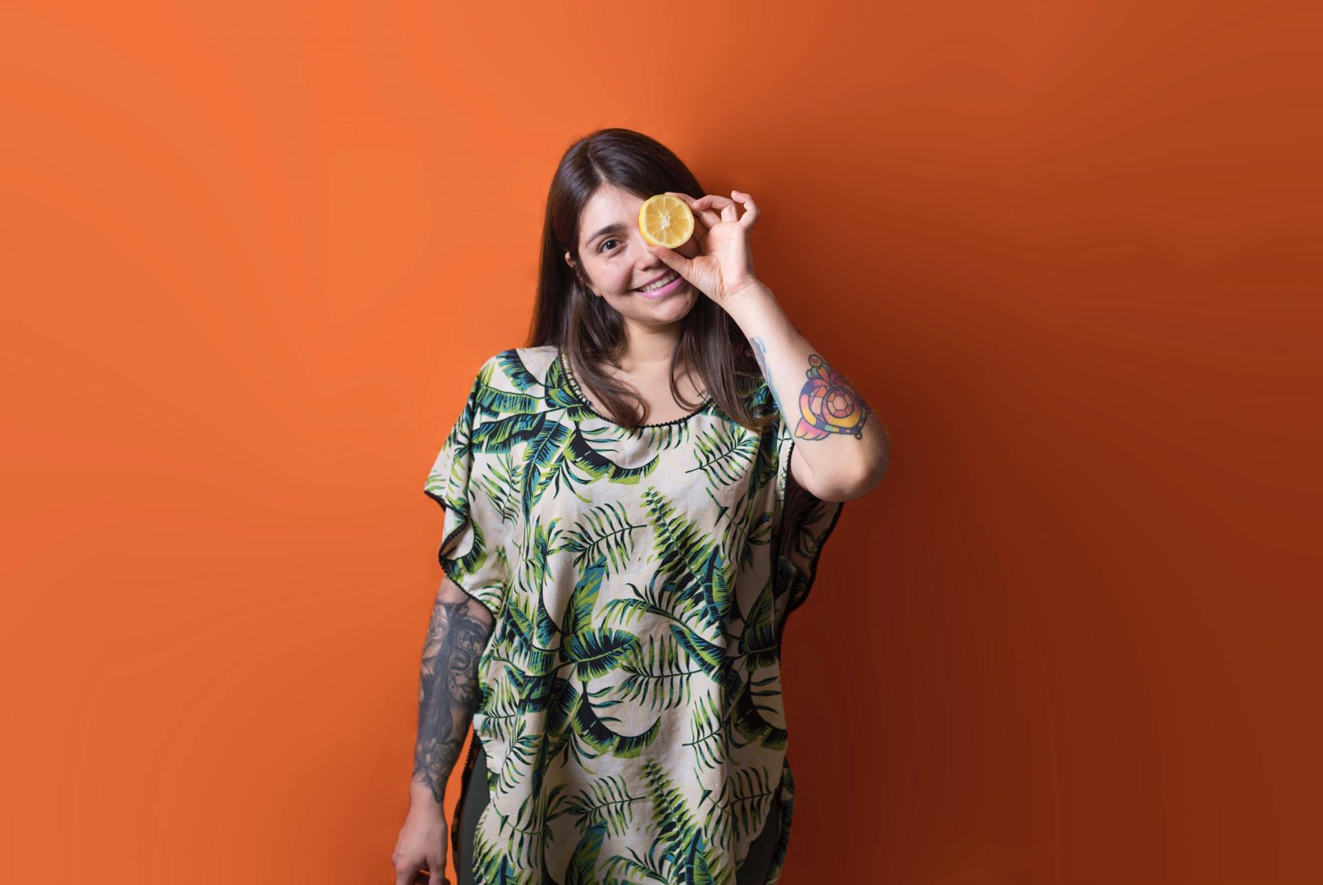 A woman is holding a slice of lemon in front of her eye.