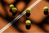 Five tennis balls on a clay court near a white line; shadows cast by sunlight.