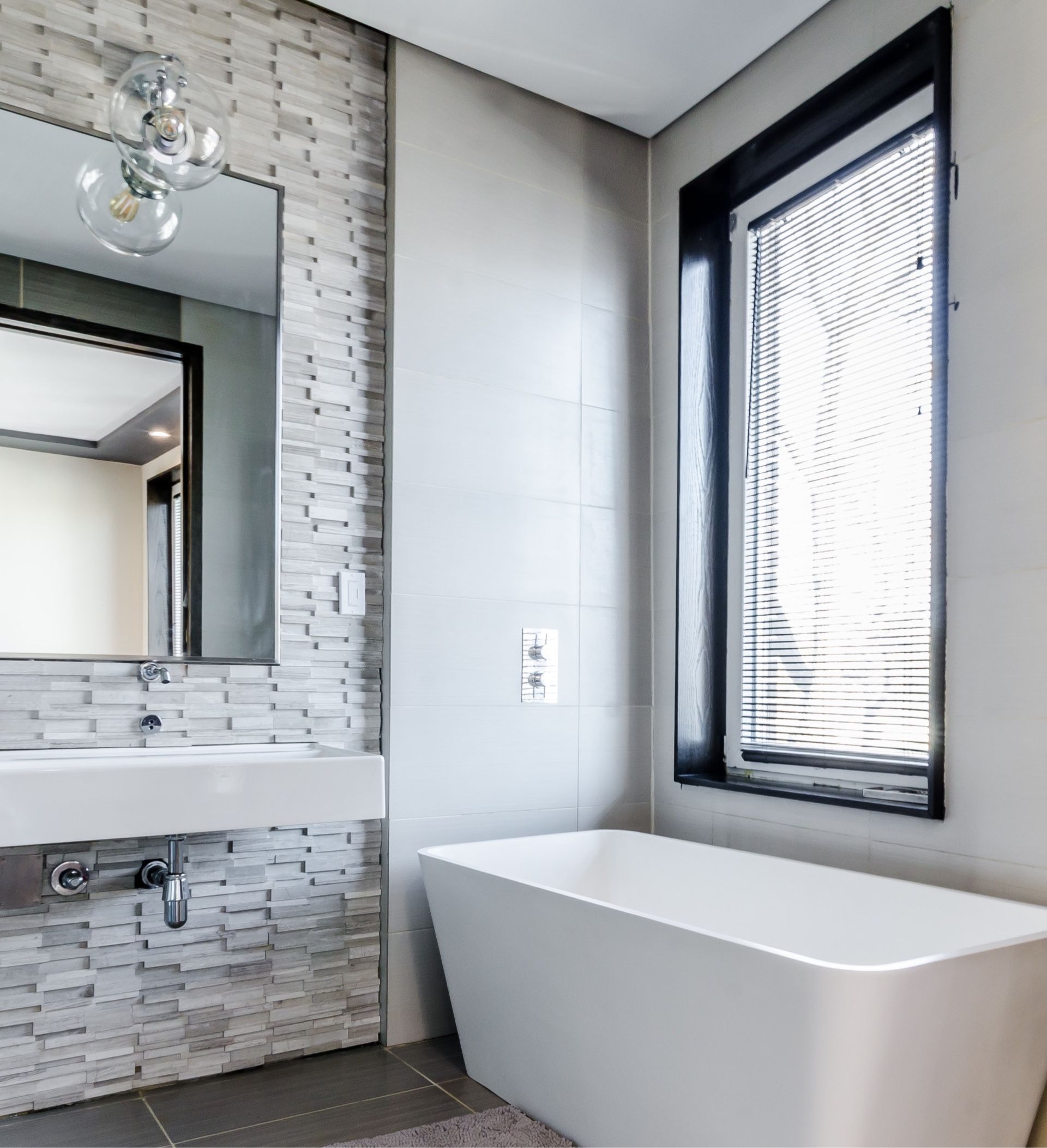Modern bathroom with floating sink, mosaic tile, and freestanding tub by a window