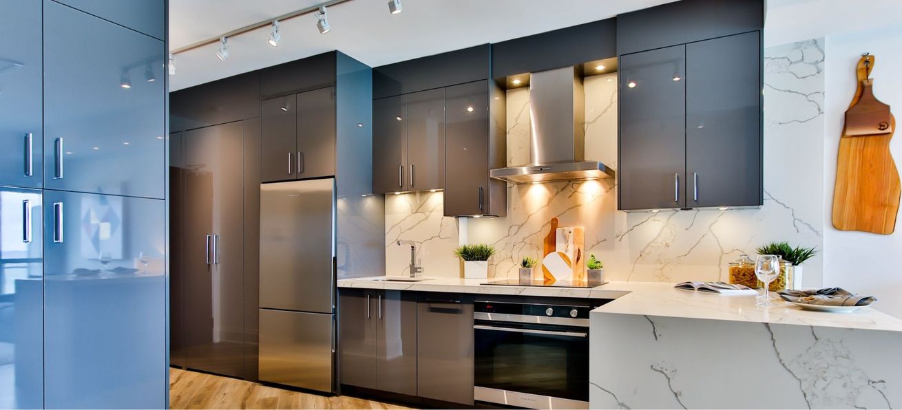 Modern kitchen with dark cabinets, marble countertops, and stainless steel appliances, lit by warm under-cabinet lighting