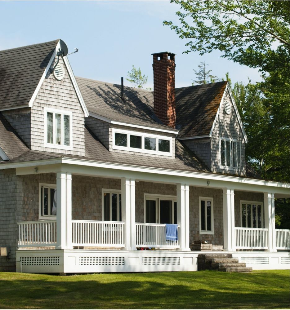 White house with gray roof, brick chimney, and front porch on a sunny lawn.