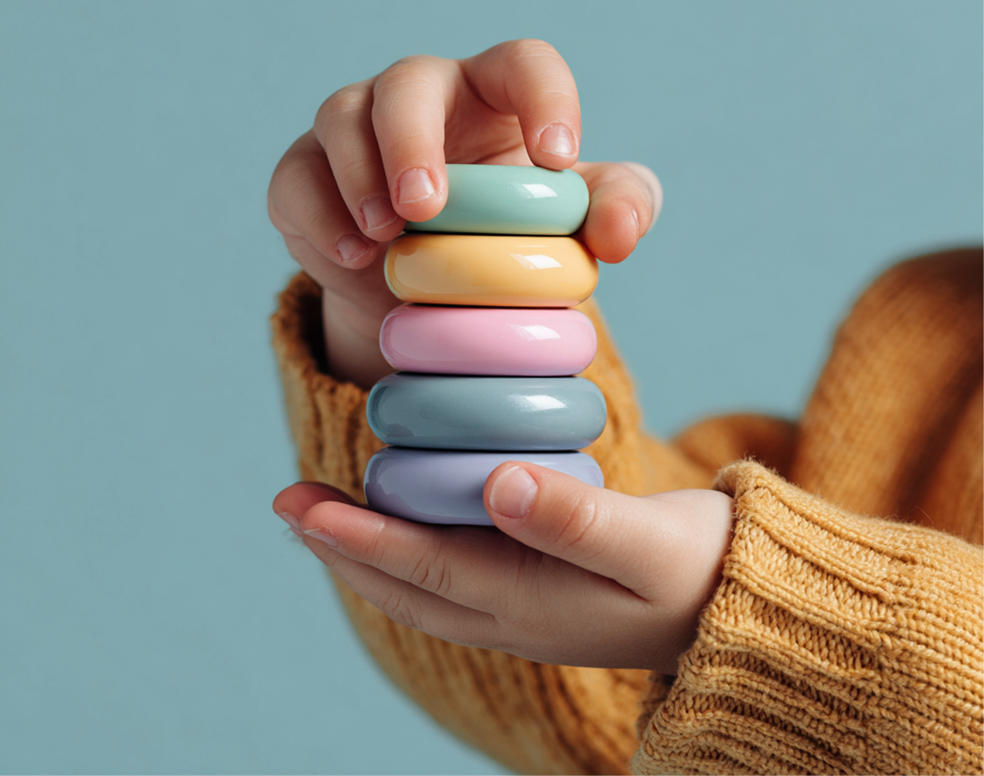 Child's hands holding a stack of colorful ring-shaped wooden toys, wearing an orange sweater, with a blue background.