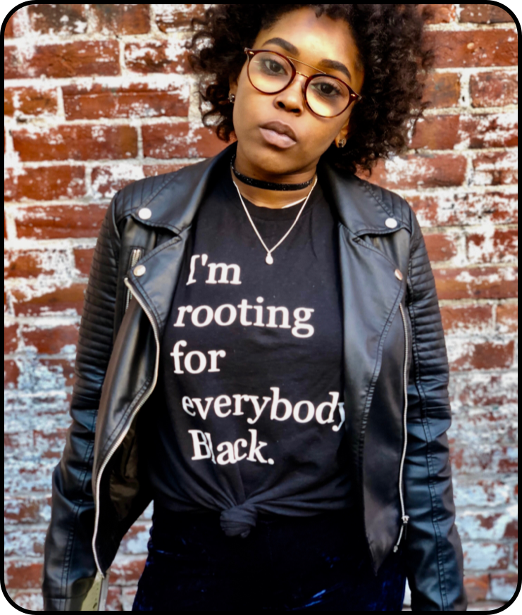 Een persoon met krullend haar, een bril, een zwarte leren jas en een T-shirt met de tekst: