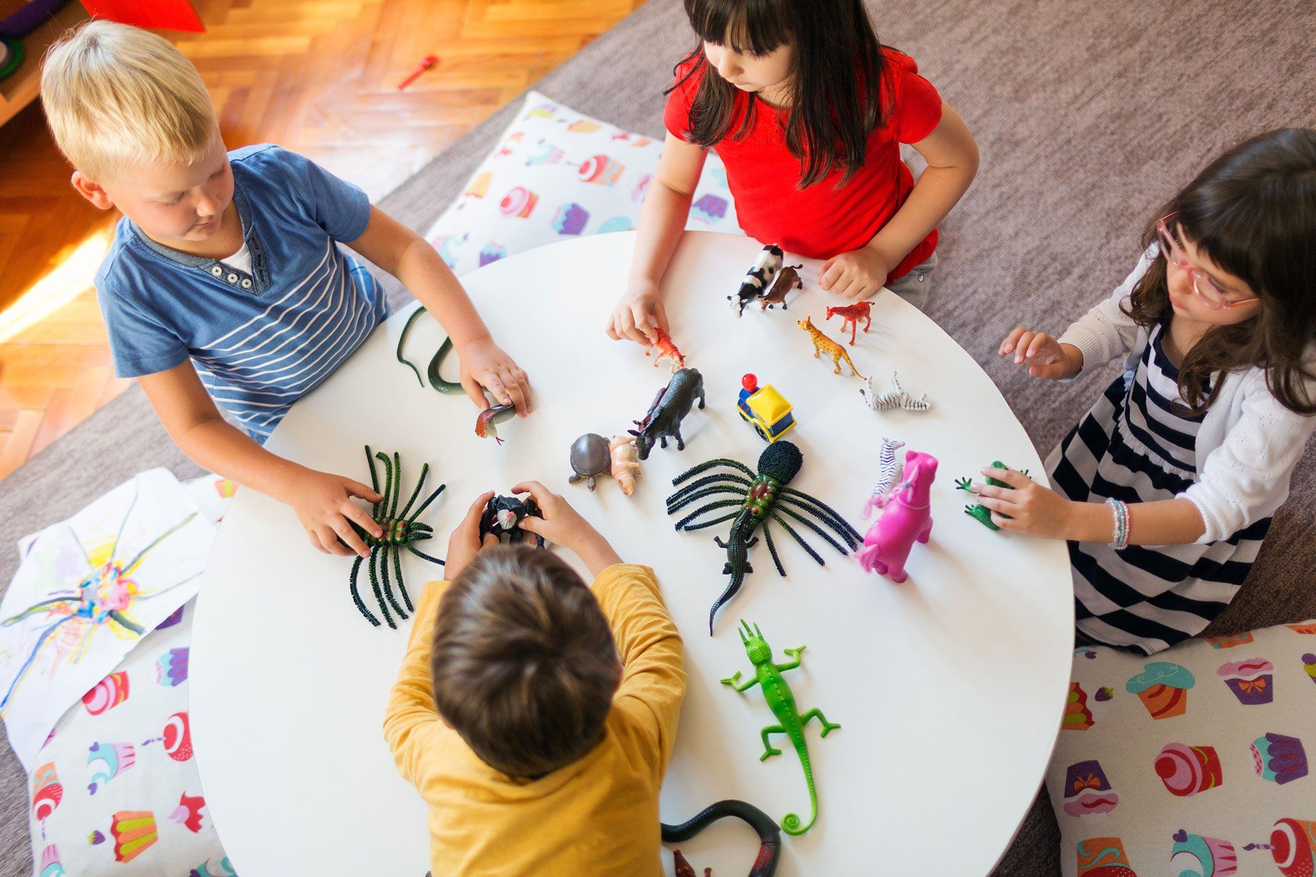 Four children playing with toy animals around a white table.
