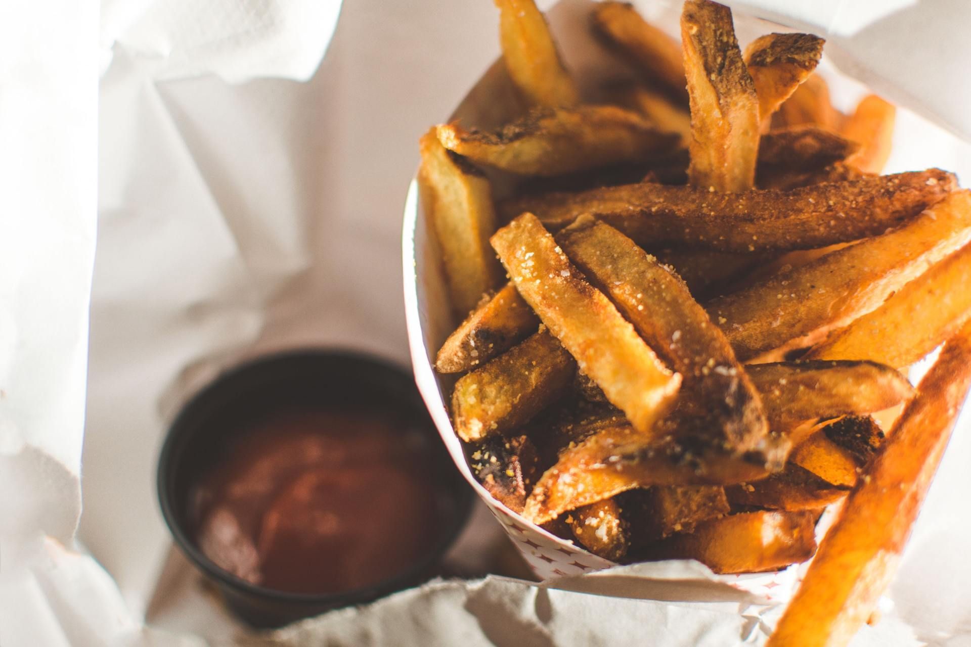 A bowl of crispy golden French fries with a small cup of ketchup on a white tablecloth.