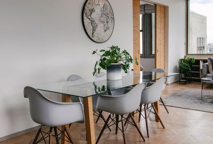 Modernes Esszimmer mit Glastisch, grauen Stühlen, Topfpflanze und großer Wanduhr