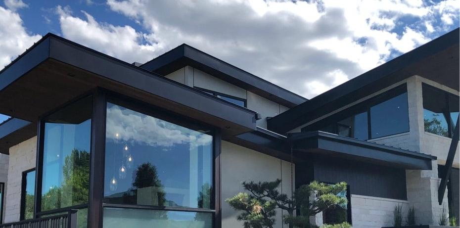 Modern house exterior with large glass windows, dark rooflines, and blue sky reflections