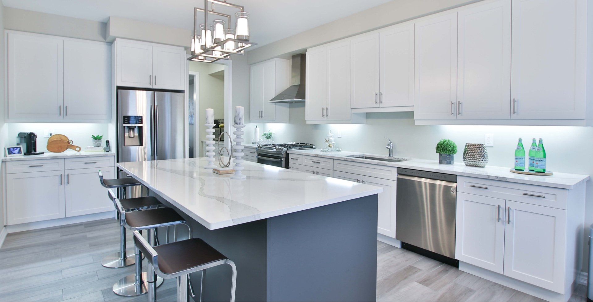 A bright, modern kitchen featuring white cabinets, a charcoal gray island with bar stools, and stainless steel appliances.