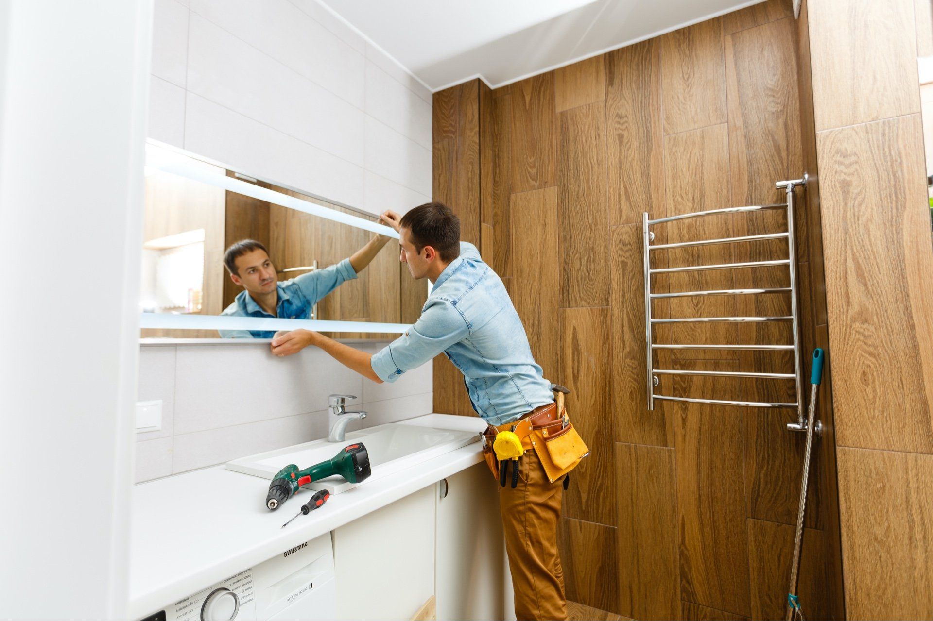 workman fixing large mirror to a bathroom wall