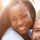 Woman smiling, close-up with warm lighting, sharing space with another person.