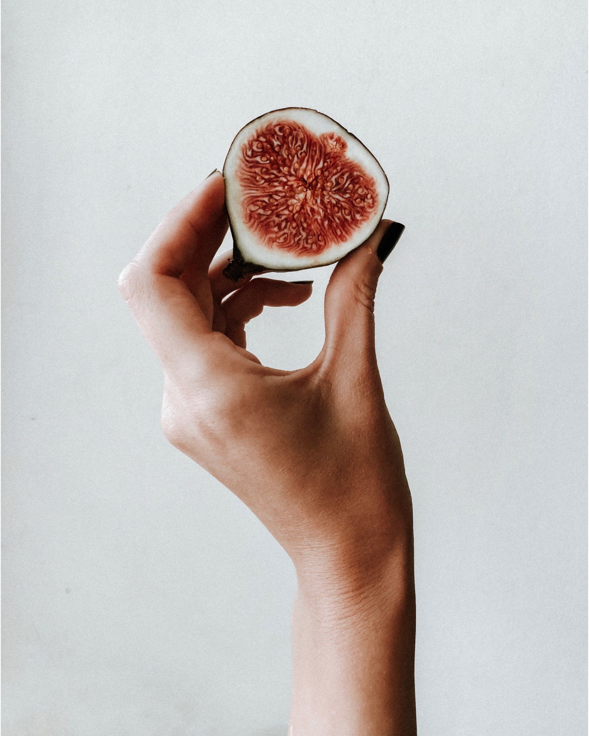 Hand holding a halved fig, showing the red interior against a white background.