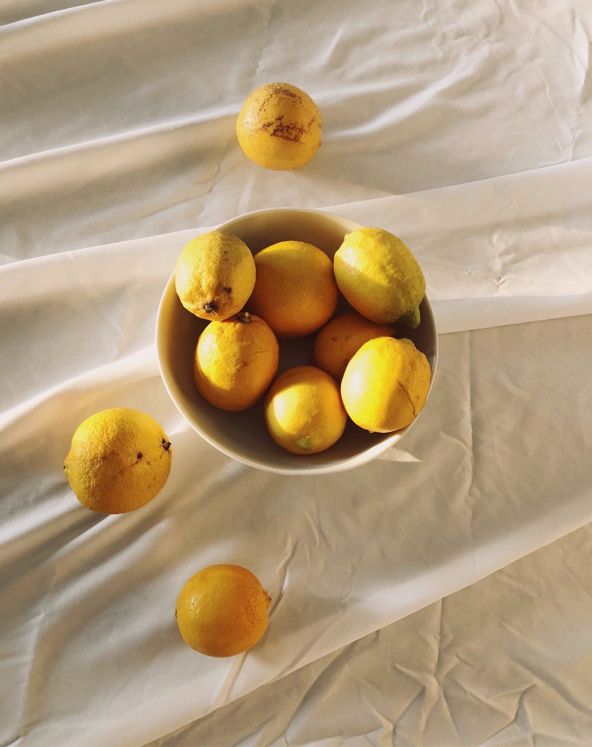 Lemons in a white bowl and scattered on white cloth.