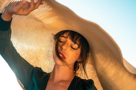 Woman in a teal top holding a wide-brimmed straw hat in bright sunlight