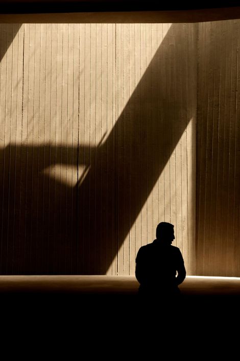 Silhouette of a person standing before a sunlit curtain with a large diagonal shadow.