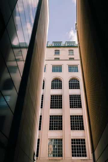 Looking up between tall buildings at a beige facade with rows of windows against a blue sky