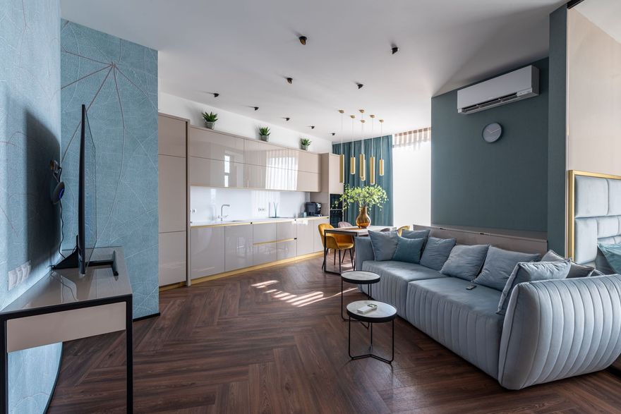 Modern open-plan living room with gray sofa, TV, kitchen, and dining area in a bright apartment