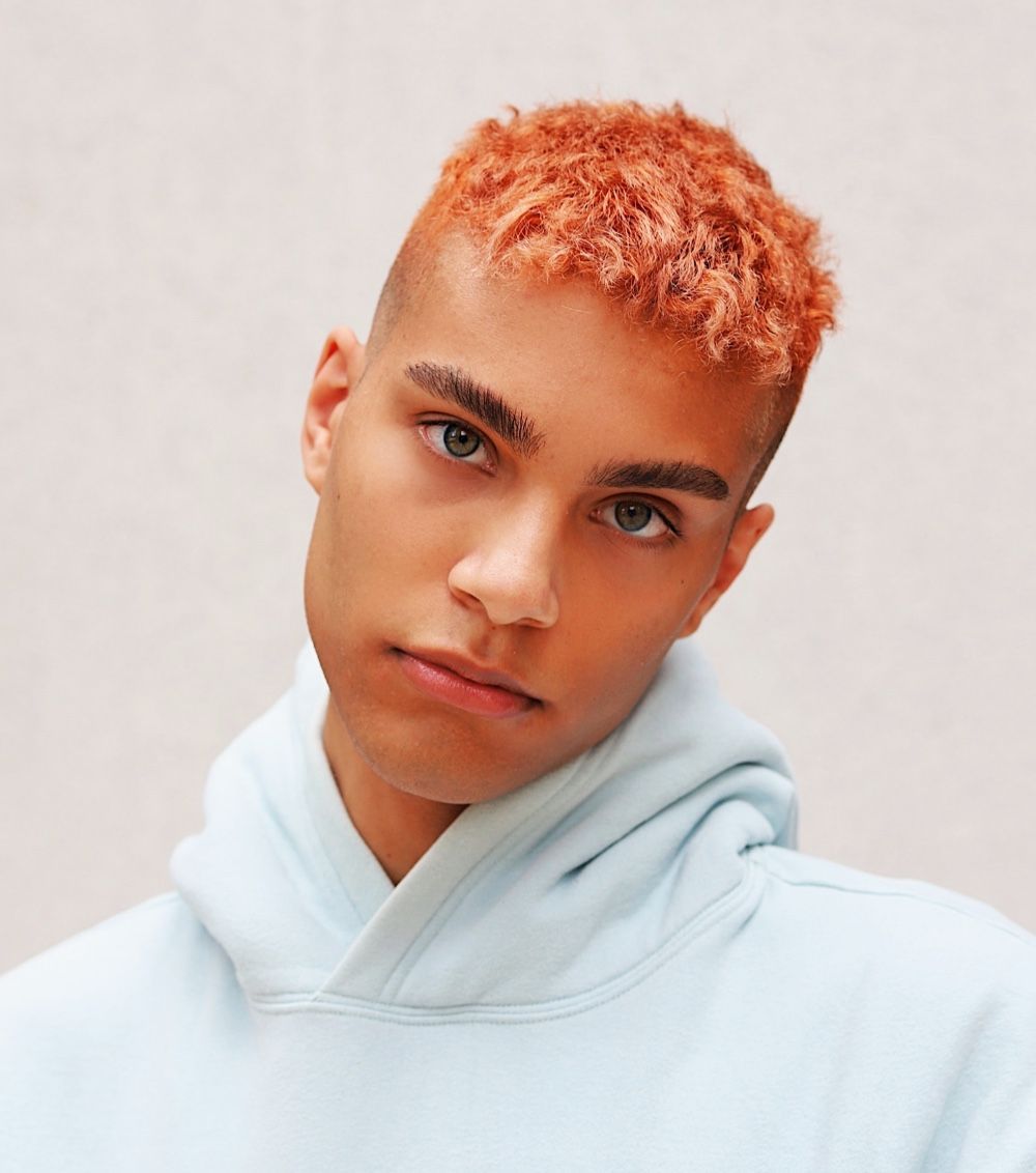 Person with orange hair wearing a light blue hoodie, looking toward the camera.