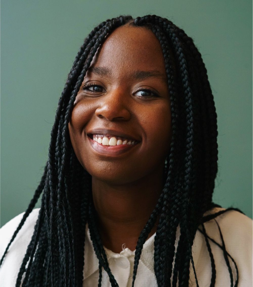 Woman with braided hair smiles in front of a green background.