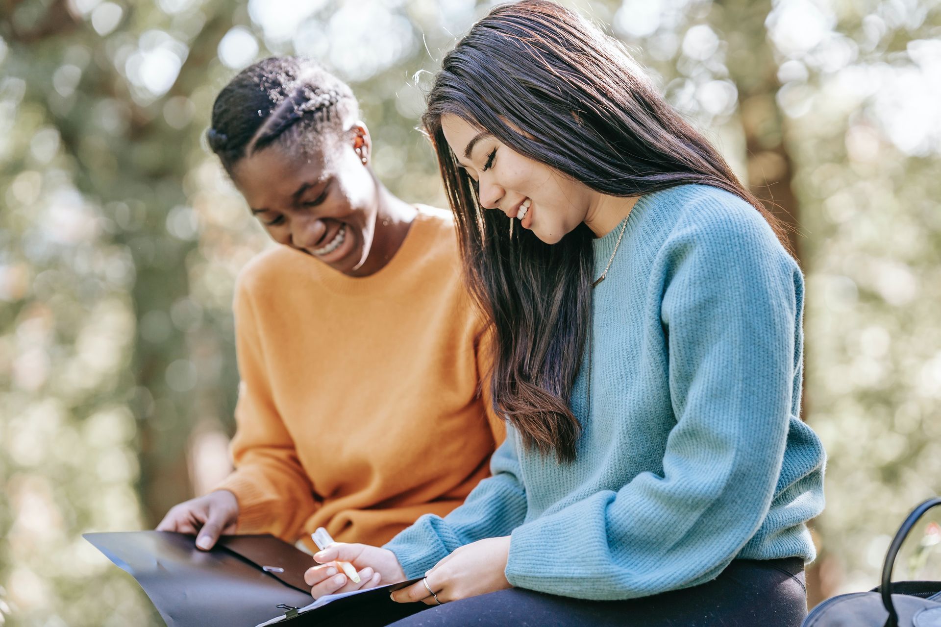 Twee vrouwen zitten naast elkaar in een park en kijken naar een laptop.