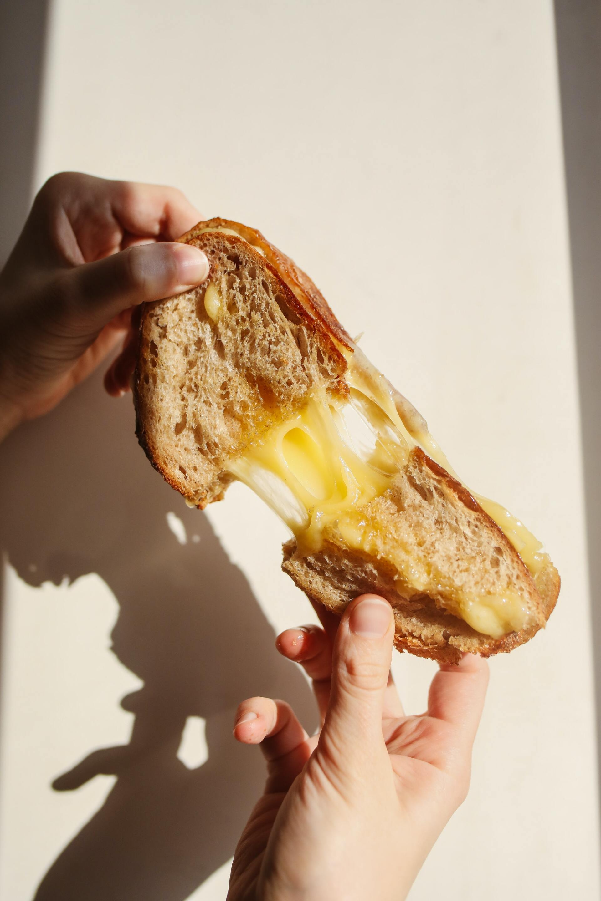 Een persoon met een gegrilde kaassandwich met gesmolten, rekbare kaas.