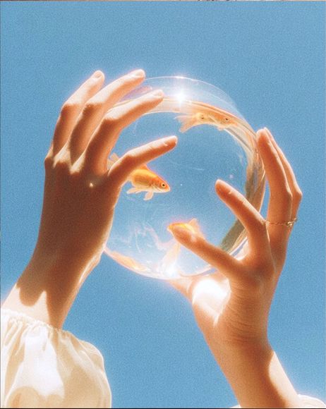Hands holding a clear glass sphere against a bright blue sky.