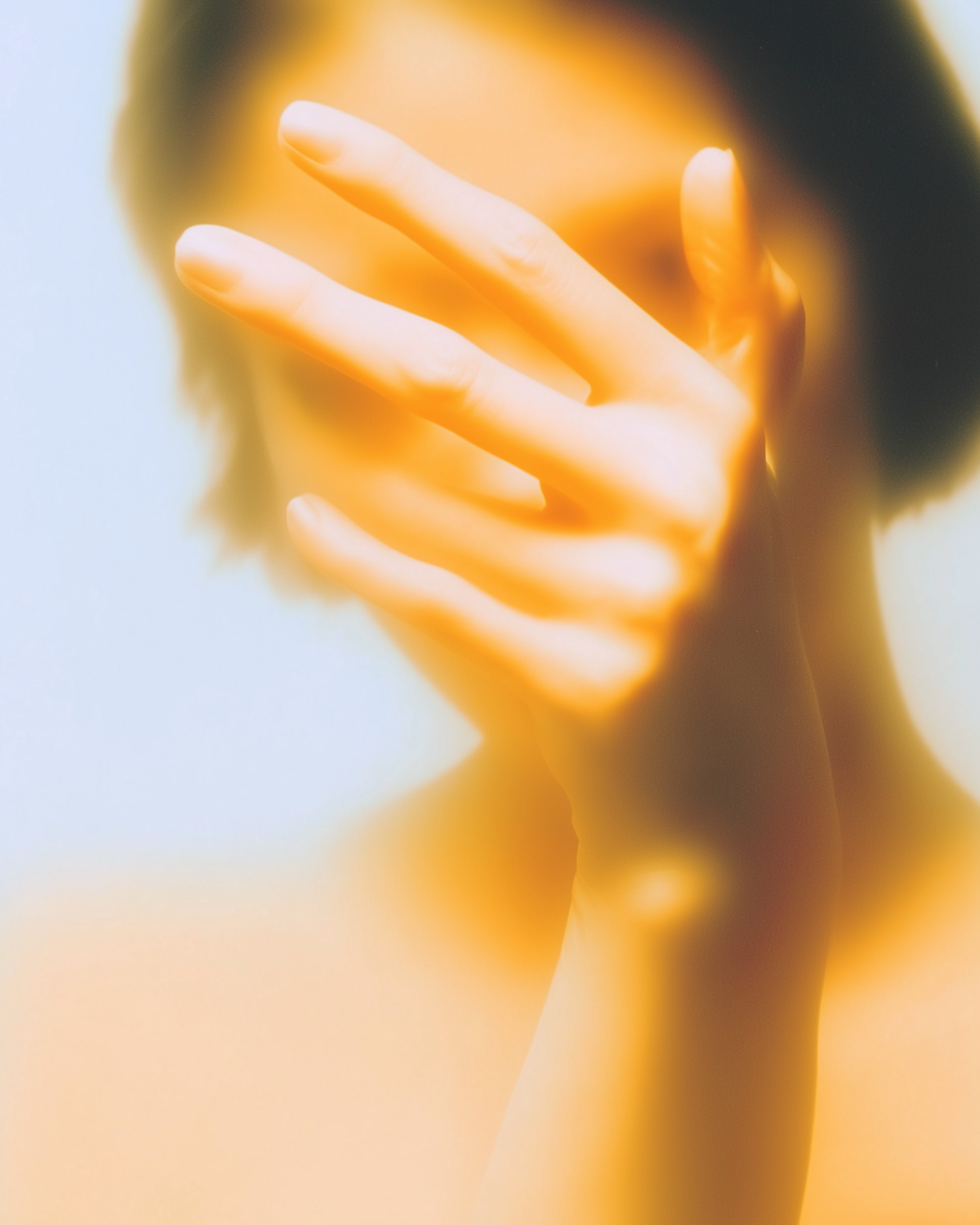 Soft-focus close-up of a hand covering part of a face in warm orange light
