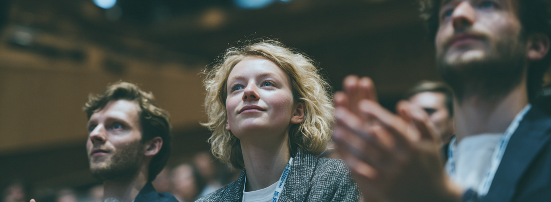 People applauding and looking up at something in an auditorium. A woman in the center smiles and looks up.