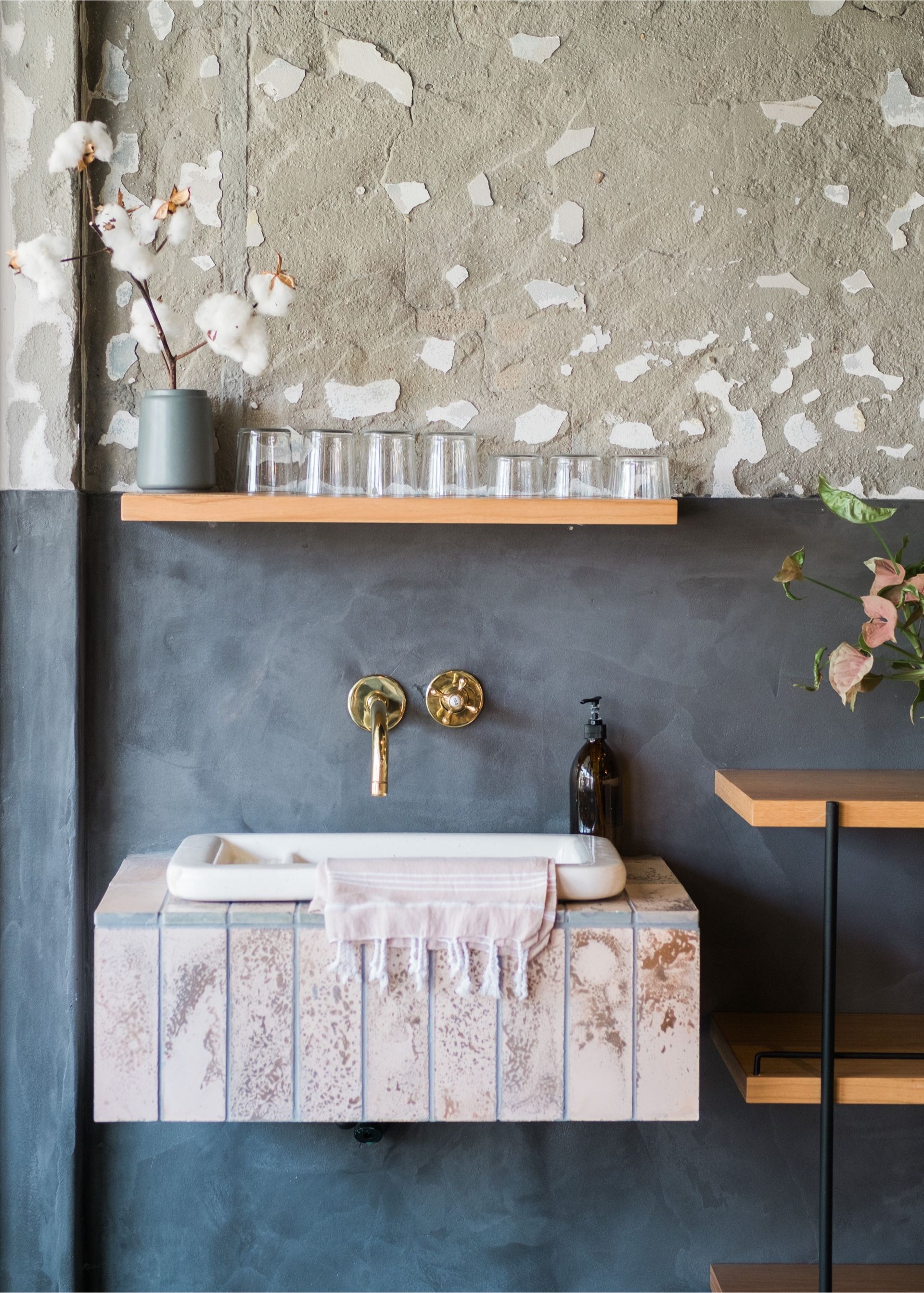 Modern bathroom vanity with marble sink, brass fixtures, and a concrete wall with open shelf.