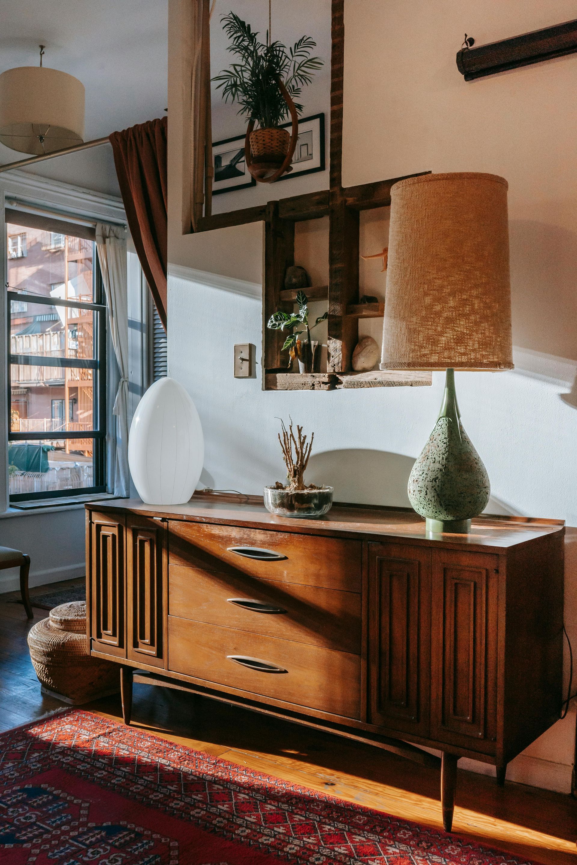 Mueble de madera con lámpara, decoración y ventana en una habitación bien iluminada.