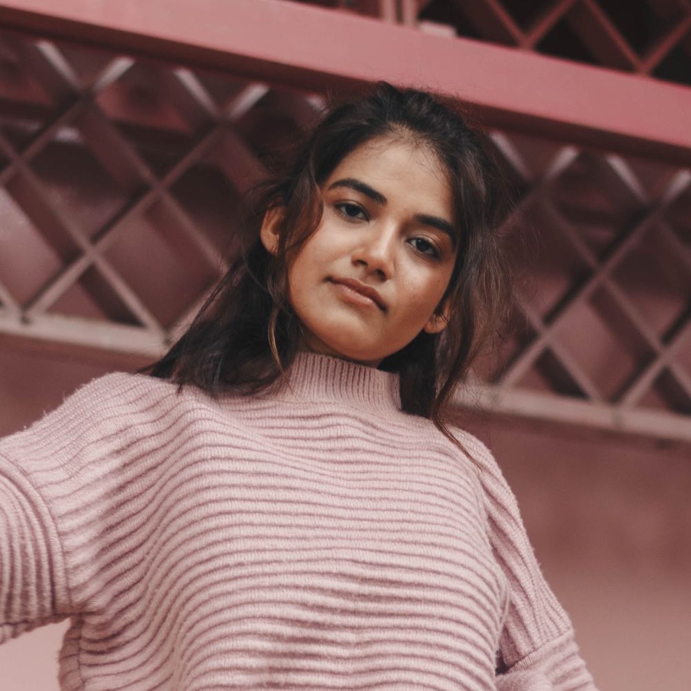 A woman is wearing a pink sweater and looking at the camera.