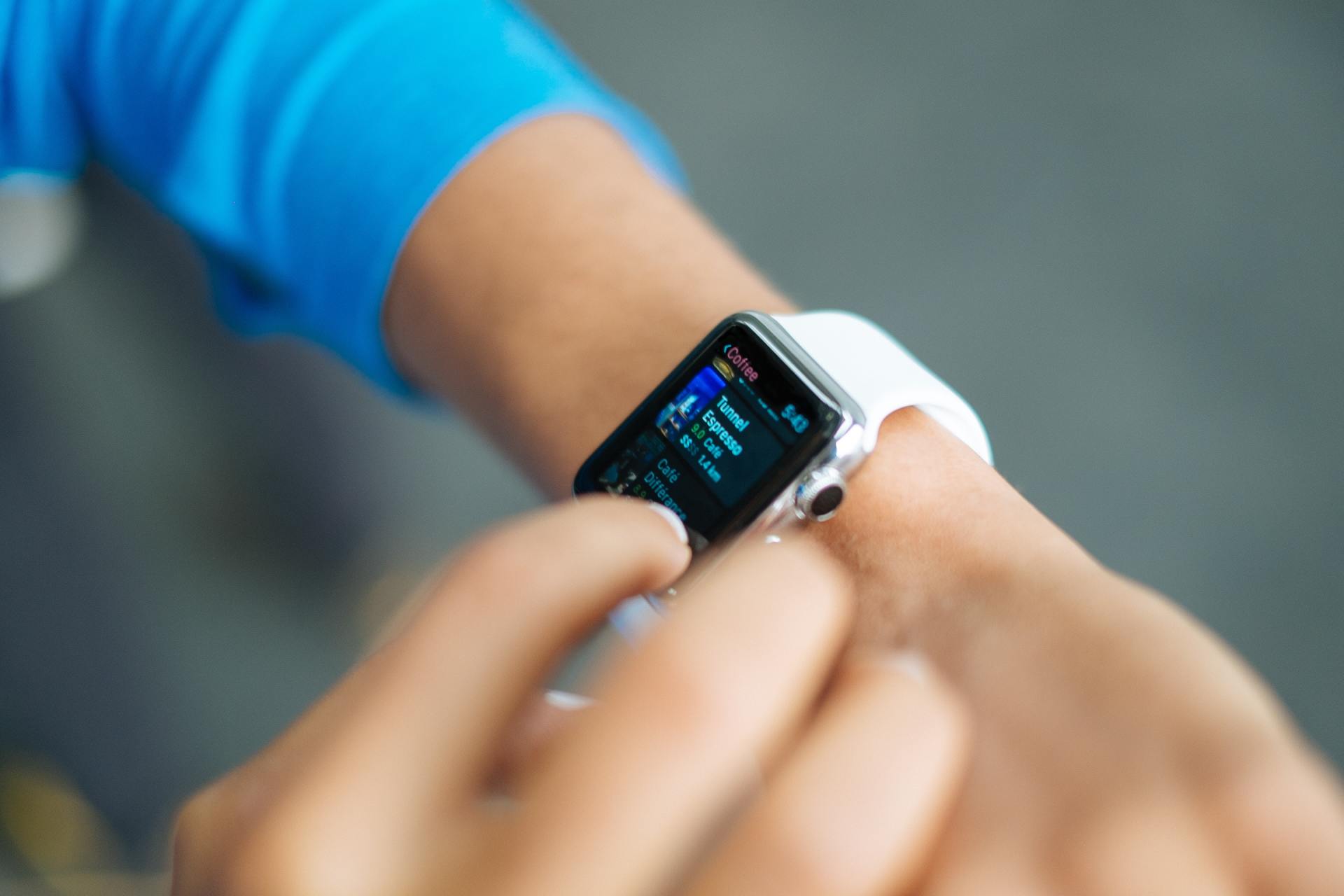 Person wearing a white smartwatch, interacting with the screen, with a blue sleeve visible.
