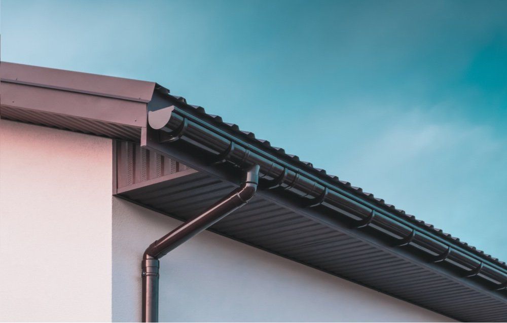 Brown rain gutter and downspout on a house, against a blue sky.