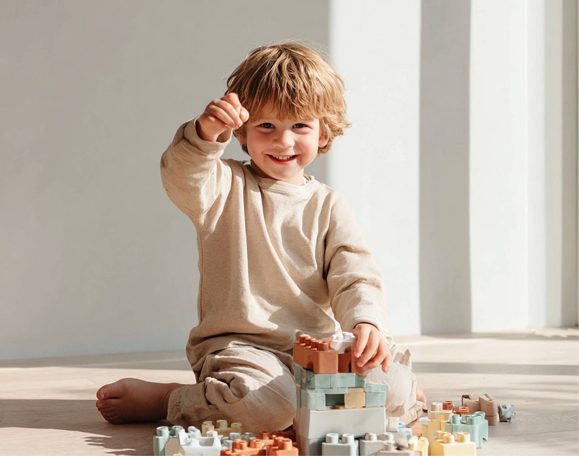 Young child playing with colorful blocks, smiling, raising hand.