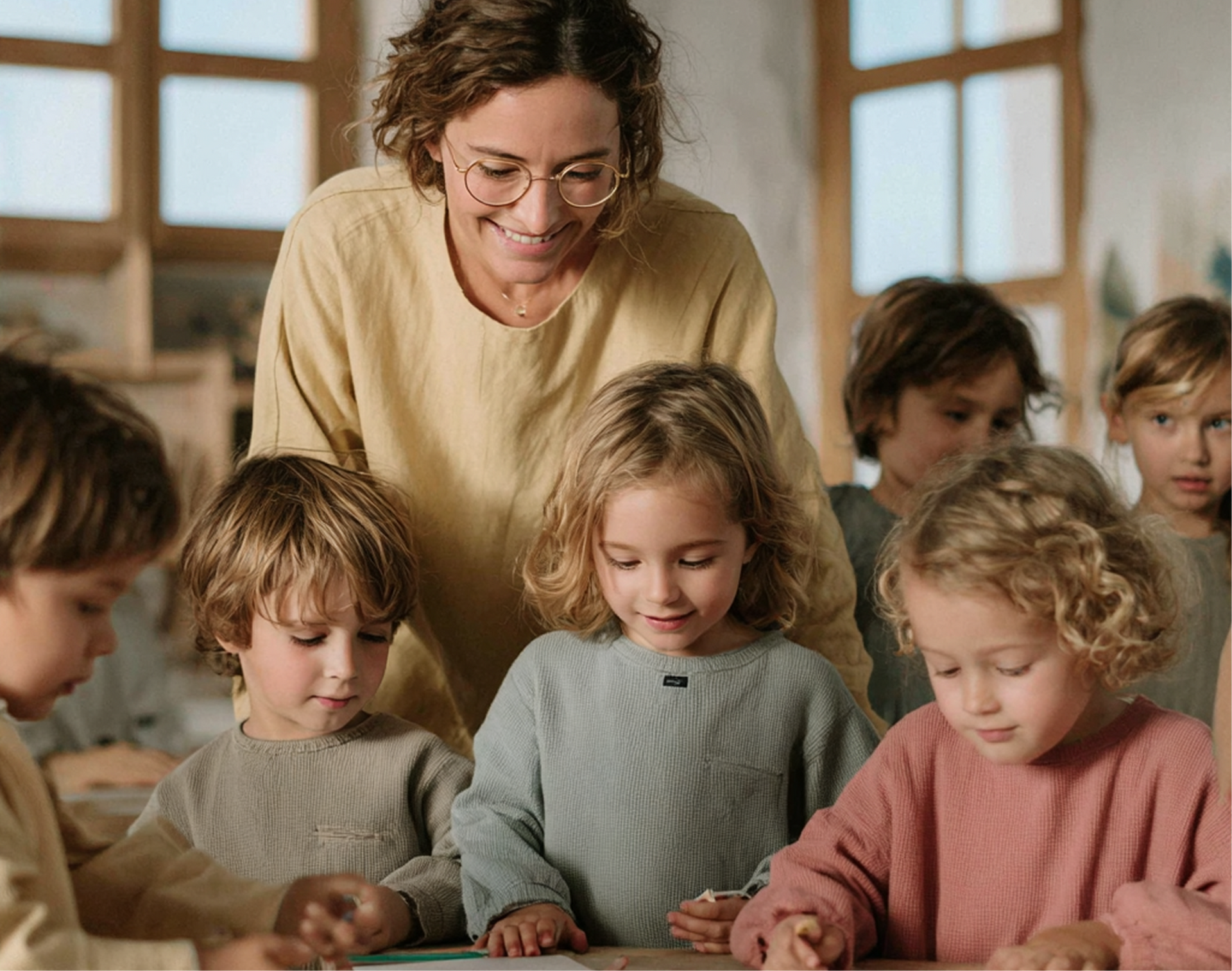 Teacher and children in a classroom, smiling while working at a table.