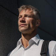 A person in a pinstriped button-down shirt looks upward against a dark, minimalist wall background.