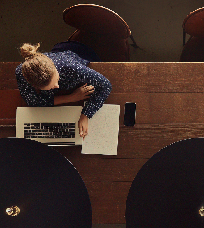 Top-down view of someone at a wooden table using a laptop and writing on a piece of paper.