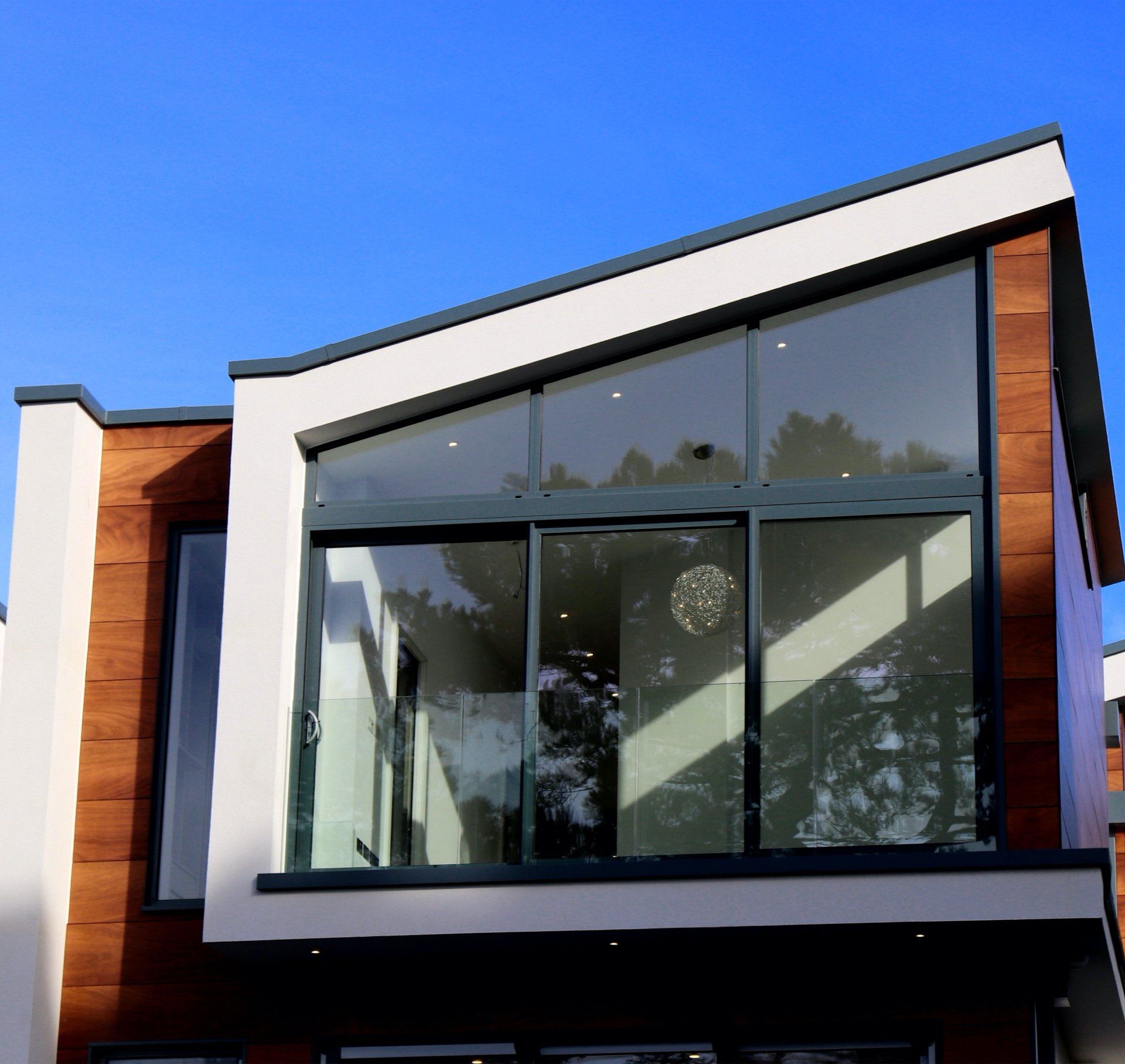 Modern house exterior with large windows, wood siding, and white trim against a blue sky.