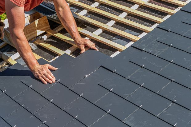 A man is installing slate tiles on a roof.
